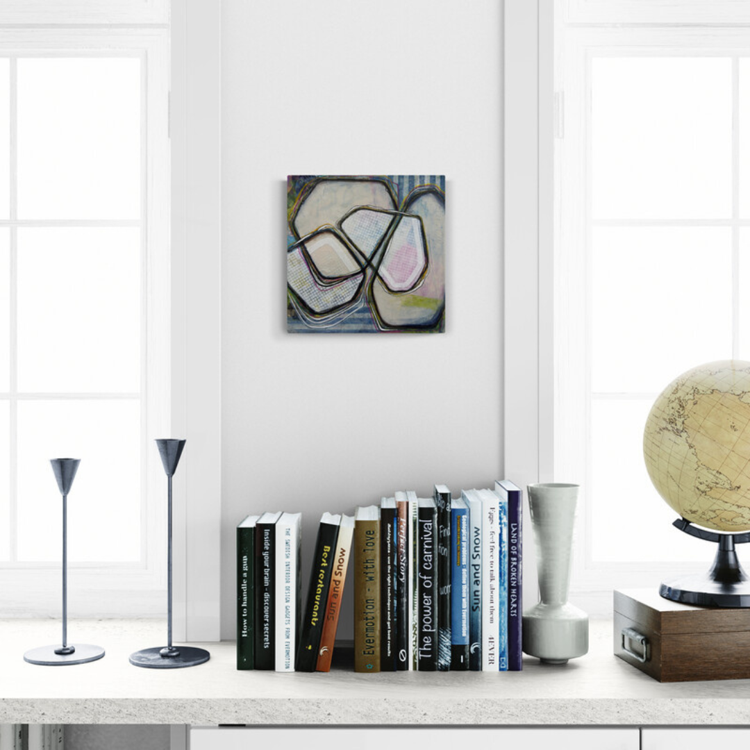 Books on a shelf with a painting above, a globe to the right, and two floor lamps on a white surface.